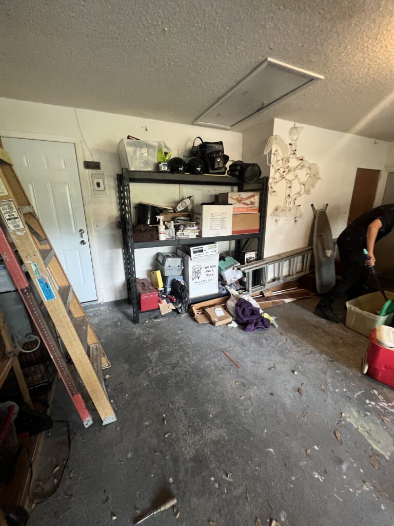 Garage with a metal shelving unit, ladders, boxes, and equipment along the wall.