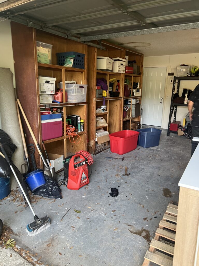 Wooden garage shelves with containers and tools, with open concrete floor space in front.